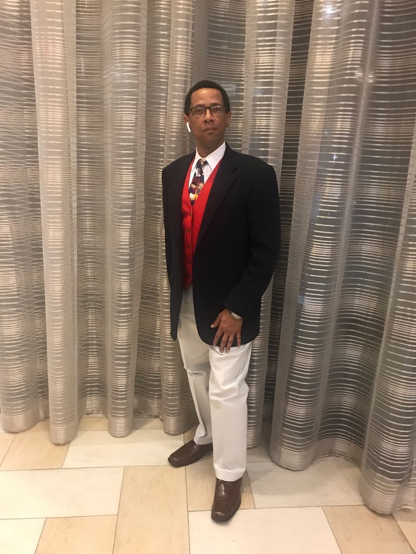 A man standing confidently in a navy blazer, red vest, and tie